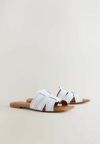 Sandales blanches à brides ouvertes avec un design à bout ouvert, matériau semblable à du cuir, semelle plate marron et détails de surpiqûres contrastantes.