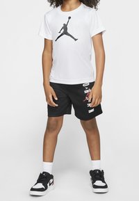 White T-shirt with black Jordan logo, black shorts with white and red lettering, black sneakers with white accents and logo, white ankle socks.