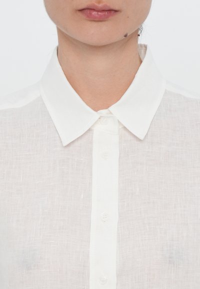 White linen blouse with a classic collar, front button closure, and a slightly textured, lightweight fabric. Visible stitching accents.