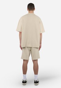 Beige teksturert kortermet skjorte og shorts sett, med en avslappet passform. Brukt med svarte og hvite joggesko og hvite sokker.