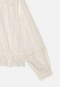 Cremefarvet bluse med teksturerede striber, puffy ærmer og elastiske manchetter. Har subtile hævede mønstre og gyldne tråd detaljer.