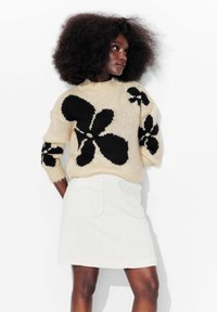 Pull en tricot épais à motifs floraux noirs, associé �à une mini-jupe en velours côtelé blanche avec deux poches arrière.