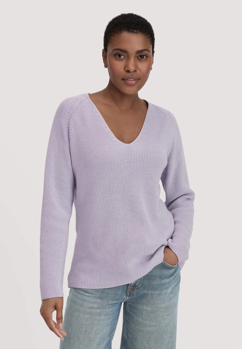Lavender gebreide trui met een V-hals en lange mouwen, voorzien van een ribbelstructuur en een relaxte pasvorm. Gecombineerd met lichtblauwe jeans.