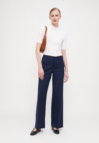 Marineblauwe wijde broek gecombineerd met een fitted wit T-shirt met korte mouwen. Accessoires zijn een bruine handtas met textuur en zwarte schoenen.