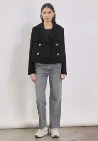 Czarna podwójnie zapinana kurtka z kołnierzem i przednimi kieszeniami z klapami; zestawiona z jasnoszarymi jeansami o prostym kroju i białymi trampkami.