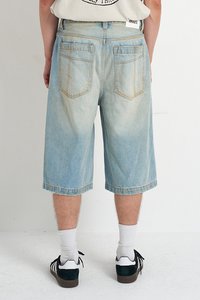 Light blue denim shorts with a loose fit, knee-length, featuring two back pockets and frayed hems. Worn with white socks and black shoes.