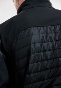 Sort jakke med en glat, blød overdel og en quilted, blank nederste sektion. Fremtrædende høj krave og minimal hardware.