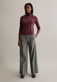 Burgundi garbópulóver, amit magas derekú, szürke csíkos, bőszárú nadrággal párosítottak. A modellen fekete csizma, ezüst nyaklánc és fonott haj látható.