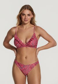 Raudonas bikinis su paisley raštu, su volangų kraštais, reguliuojamomis petnešomis ir trikampiu viršumi. Audinys yra glotnus.