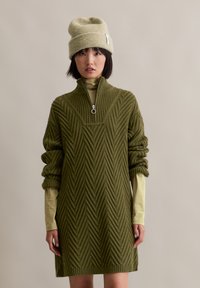 Robe en tricot vert olive avec un col montant et une texture en zigzag. À associer avec un bonnet vert clair. Manches longues et design décontracté.