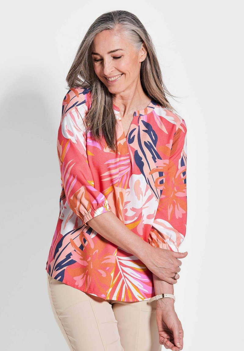 Bunte Blumenbluse mit rundem Ausschnitt, gerafften 3/4-Ärmeln und lässiger Passform. Überwiegend rosa mit Akzenten in Orange und Marineblau.