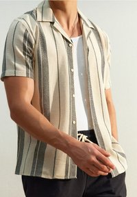 Korte mouw button-up shirt in beige met zwarte verticale strepen. Gestructureerde stof, spread collar, zichtbare knopen, gecombineerd met een effen witte onderhemd.