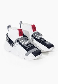 Sneakers alte bianche, nere e grigie con loghi rossi di Spider, lacci a strisce e suole bianche spesse, presentate affiancate su uno sfondo bianco.