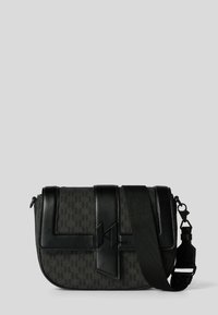 Svart axelväska med texturerat tyg, läderdetaljer, en framflik och justerbar rem. Innehåller en logodetalj och silverfärgad metall.