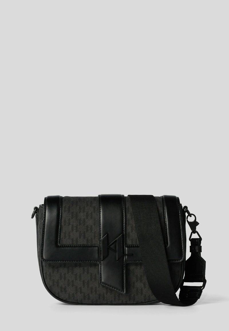 Svart axelväska med texturerat tyg, läderdetaljer, en framflik och justerbar rem. Innehåller en logodetalj och silverfärgad metall.