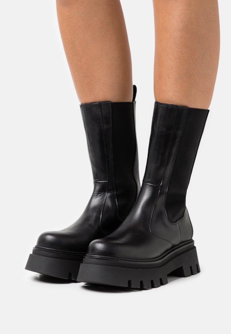 Bottines en cuir noir avec panneaux élastiques sur les côtés, semelle plateforme en caoutchouc épaisse et bout arrondi. Texture lisse et détails de couture minimaux.