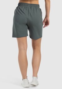 Pantalones cortos deportivos de color verde oscuro con una banda elástica en la cintura, textura suave y longitud por encima de la rodilla. Sin patrones ni acentos visibles.