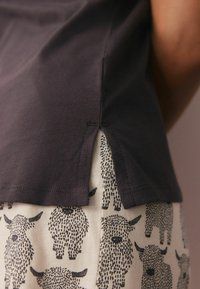 Donkergrijze katoenen t-shirt met splitten aan de zijkanten, gecombineerd met een crèmekleurige rok met zwarte geïllustreerde schapenpatronen. Soepele textuur, casual pasvorm.