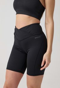 Zwarte high-waisted shorts van rekbaar materiaal met een gladde textuur, voorzien van een overlappend ontwerp en subtiele branding aan de zijkant.