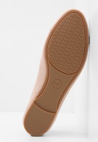 Semelle de chaussure en caoutchouc beige, dotée d'un motif texturé et d'un logo en relief. Les bords lisses et une légère courbe rehaussent la forme globale.