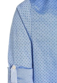 Camisa azul claro con lunares azules claros. Presenta un puño abotonado con un patrón de rayas y una manga enrollada. Textura de tela suave.