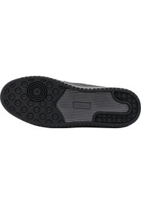 Semelle de sneaker noire présentant des motifs de prise circulaires et texturés, avec une section centrale lisse et un détail de contraste le long du bord.