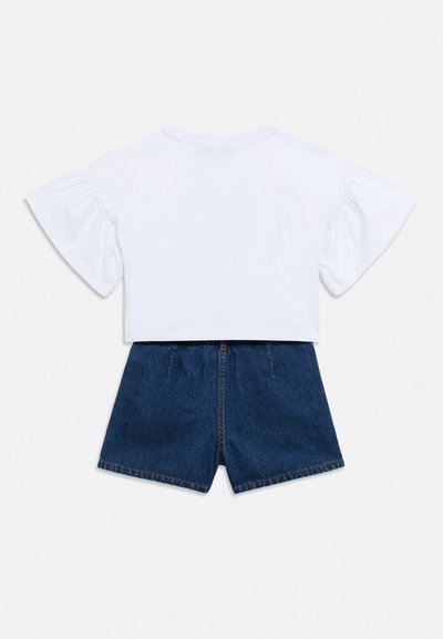 Fehér, rövid ujjú felső púpos ujjakkal, sötétkék farmer rövidnadrággal párosítva, hátulnézetben, fehér háttéren elhelyezve.