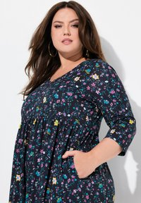Schwarzes Blumenkleid mit langen Ärmeln, das mehrfarbige Blumen und eine geraffte Taille aufweist. Verfügt über seitliche Taschen für zusätzliche Funktionalität.
