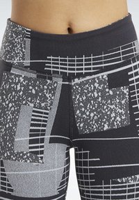 Czarne legginsy z geometrycznym wzorem w odcieniach szarości, z różnorodnymi fakturami, w tym plamkowymi i prążkowanymi wzorami, oraz wysokim pasem.