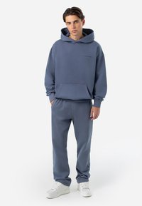 Light blue hooded sweatshirt with front pocket, paired with matching sweatpants. White sneakers complete the relaxed outfit.
