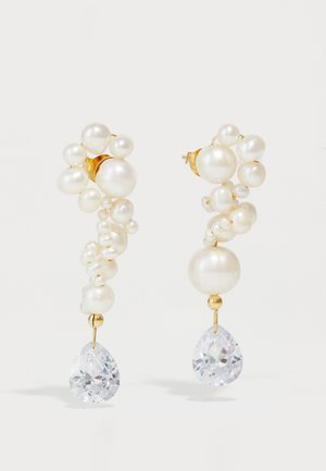 Pendientes en tono dorado con perlas blancas agrupadas y cristales transparentes en forma de lágrima. Superficies lisas y texturizadas crean un contraste visual y profundidad.