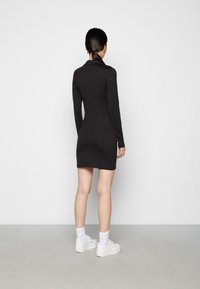 Black long-sleeve dress with a fitted silhouette, featuring a collared neck. Paired with white sneakers and visible ankle socks.