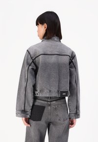 Grå denim cropped jakke med kragehals, synlig søm og logo på baksiden. Kombinert med grå denim bukser med et lapp.
