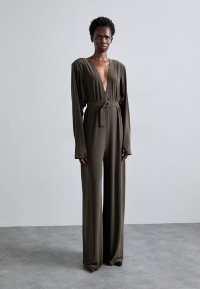 Salopetă cu mâneci lungi de culoare verde măslinie, cu un decolteu adânc în formă de V, strânsă în talie cu un brâu cu cataramă rotundă. Design cu pantaloni evazați.
