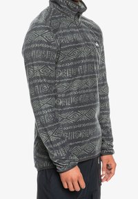 Szary polarowy półgolf z wysokim kołnierzem, zdobiony geometrycznym wzorem w jasnoszarym kolorze. Zamek błyskawiczny z przodu oraz logo na górnej części klatki piersiowej.