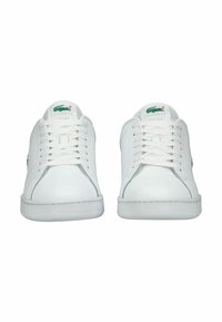 Bílé kožené tenisky s plochou podrážkou, šněrováním vpředu a vyšívaným zeleným logem na boku. Hladký povrch s minimalistickým designem.