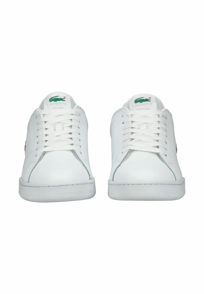 Baskets en cuir blanc avec une semelle plate, un laçage à l'avant et un logo vert brodé sur le côté. Texture lisse avec un design minimaliste.