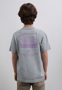 T-shirt en coton gris clair avec un graphisme violet d'un sandwich accompagné de texte et d'un design de crâne au dos. Manches courtes et coupe décontractée.