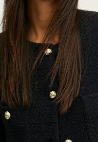 Marinen textured jacket med fremtrædende guldtonede knapdetaljer. Nærbillede, der fremhæver knapdetaljer og stoftekstur.