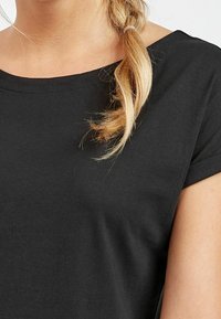 Czarny top z krótkim rękawem i szerokim dekoltem, wykonany z miękkiego bawełnianego materiału, o gładkiej fakturze i luźnym kroju.