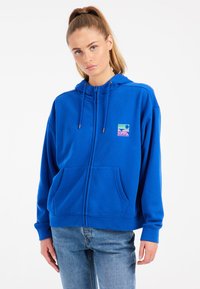 Sudadera azul con cremallera en material suave y bolsillo frontal. Presenta un colorido logo gráfico en el pecho y capucha con cordón.