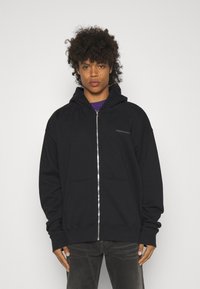 Czarna bluza z kapturem na zamek, wykonana z miękkiego materiału, z przednią kieszenią, regulowanym kapturem i subtelnym logo na klatce piersiowej.