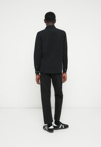 Camisa negra de manga larga con cuello, combinada con pantalones negros y zapatillas negras con rayas blancas. Diseño simple y entallado.