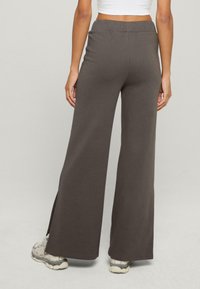 Ciemnoszare spodnie typu wide-leg z miękkiego, elastycznego materiału. Wyraźne rozcięcia po bokach u dołu. Elastyczny pas dla wygody.