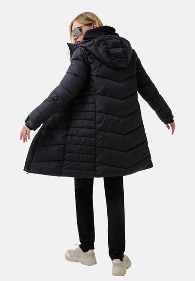 Black puffer coat with a hood, featuring chevron stitching, zip pockets, and a flared hem. Worn over black trousers and white sneakers.
