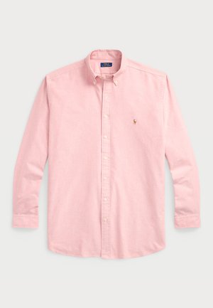 Camisa de botones de color rosa pálido con un cuello clásico, mangas largas y un pequeño logotipo bordado en el lado izquierdo del pecho. Tela de algodón, textura suave.