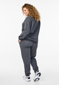 Sudadera gris oscuro y pantalones de chándal a juego, hechos de una tela suave, con un corte relajado y puños elásticos, combinados con zapatillas deportivas en negro y blanco.