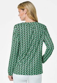 Langärmlige Bluse in einem grünen, schwarzen und weißen geometrischen Muster. Geschmeidiger Stoff mit einem runden Ausschnitt und Raffung am Rücken.