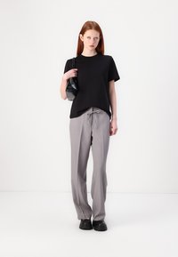 Sort kortærmet t-shirt parret med lysegrå bukser med snoretræk. Modellen holder en lille sort håndtaske og har sorte sko på.