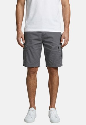 Homme portant un short cargo gris, un t-shirt blanc et des baskets blanches, debout avec les bras détendus le long du corps sur un fond uni.